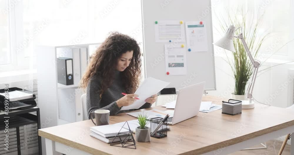 Businesswoman examining documents and writing notes at office desk Businesswoman examining documents and writing notes at office desk