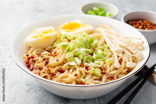 Asian soup ramen with noodles, spring onion, enoki mushrooms and boiled egg in bowl on concrete background. Selective focus.