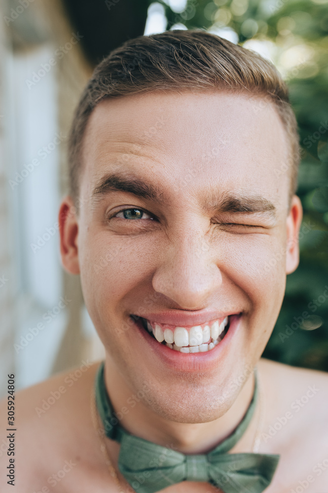 Closeup portrait of a young and smiling man with a green bow-tie. A bright smile on the face of a young groom. Emotional photography and winking. Morning businessman. Closeup portrait of a young and smiling man with a green bow-tie. A bright smile on the face of a young groom. Emotional photography and winking. Morning businessman.