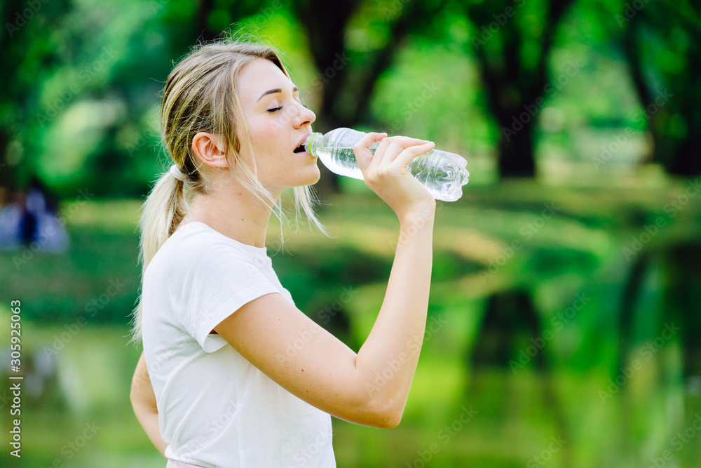 Caucasian woman thirsty and drinking water from pet bottle in public park Caucasian woman thirsty and drinking water from pet bottle in public park