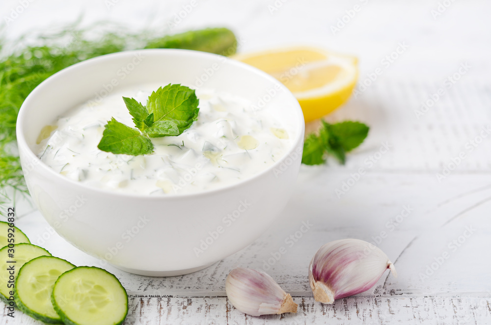 Greek dip sauce or dressing tzatziki decorated with olive oil and mint on white wooden table. Greek dip sauce or dressing tzatziki decorated with olive oil and mint on white wooden table.