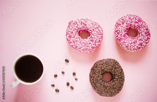 delicious donuts with pink icing and powder with a cup of aromatic coffee on a white wooden background.