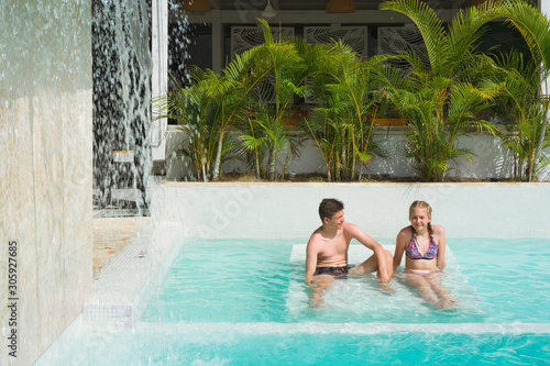 Caucasian teenagers sitting on the bed and relaxing in swimming pool in luxury hotel, Punta Cana, Dominican Republic. Artificial waterfall on the left. Summer vacation concept © Mariusz Świtulski