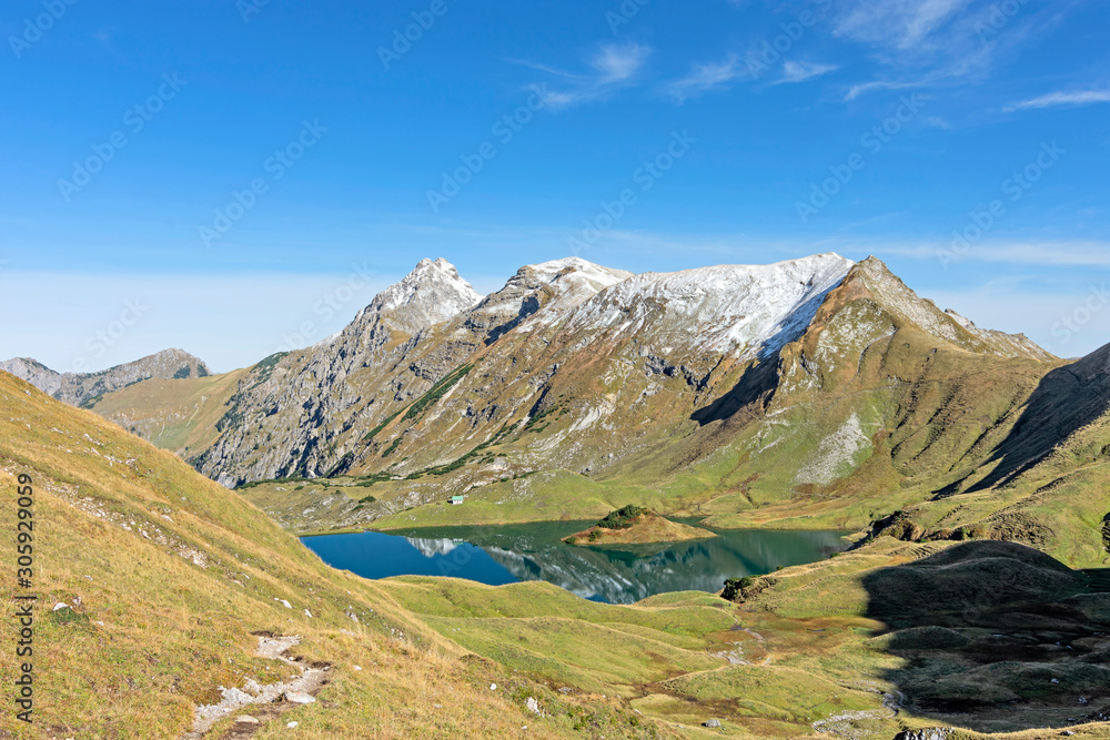Idyllic mountain lake Schrecksee in autumn (Allgaeu Alps, Bavaria, Germany). Alpine landscape with green grass, rocky mountains and some snow under blue sky.