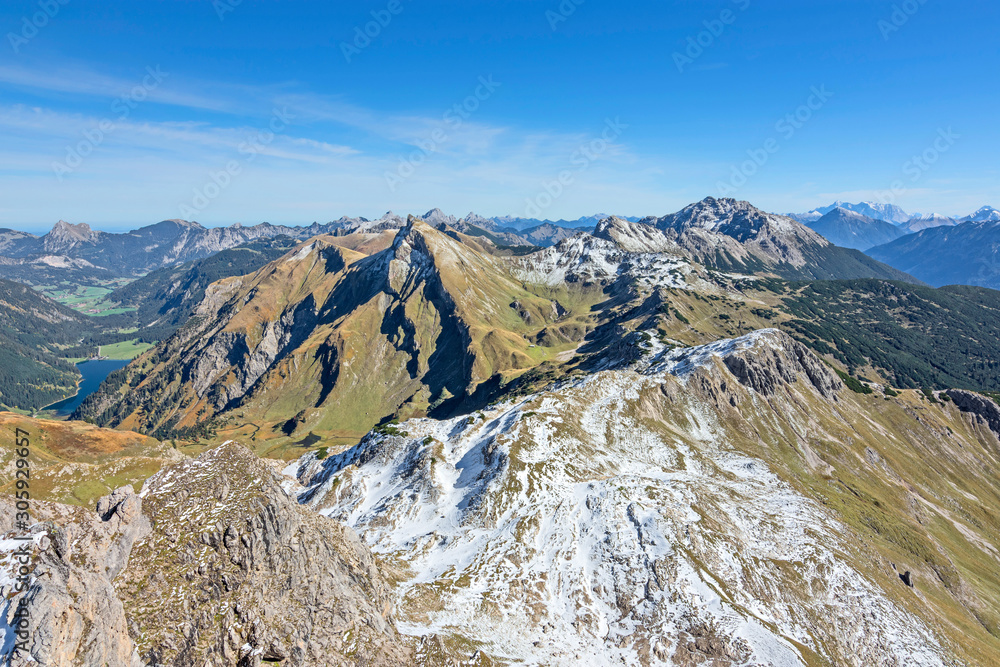 View from the summit of a mountain at a beautiful day in autumn to the Allgau Alps (Tyrol, Austria). Alpine landscape with rocky mountains, colorful pastures, blue sky.