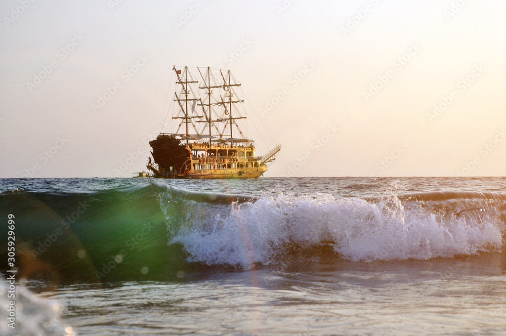 Obraz premium Tropical sunset background. Beautiful colorful ocean wave. Pleasure ship with masts on the horizon.
