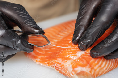 Chef man wearing gloves removes the bones from the salmon fillet closeup.