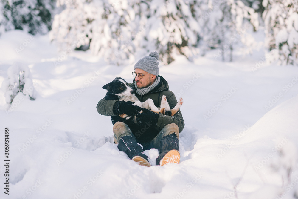Happy man holding lovely dog in his hands in snowy forest. Smiling boy hugging adorable puppy in winter wood. Pet lover. Dog - human`s friend concept. Happy man holding lovely dog in his hands in snowy forest. Smiling boy hugging adorable puppy in winter wood. Pet lover. Dog - human`s friend concept.