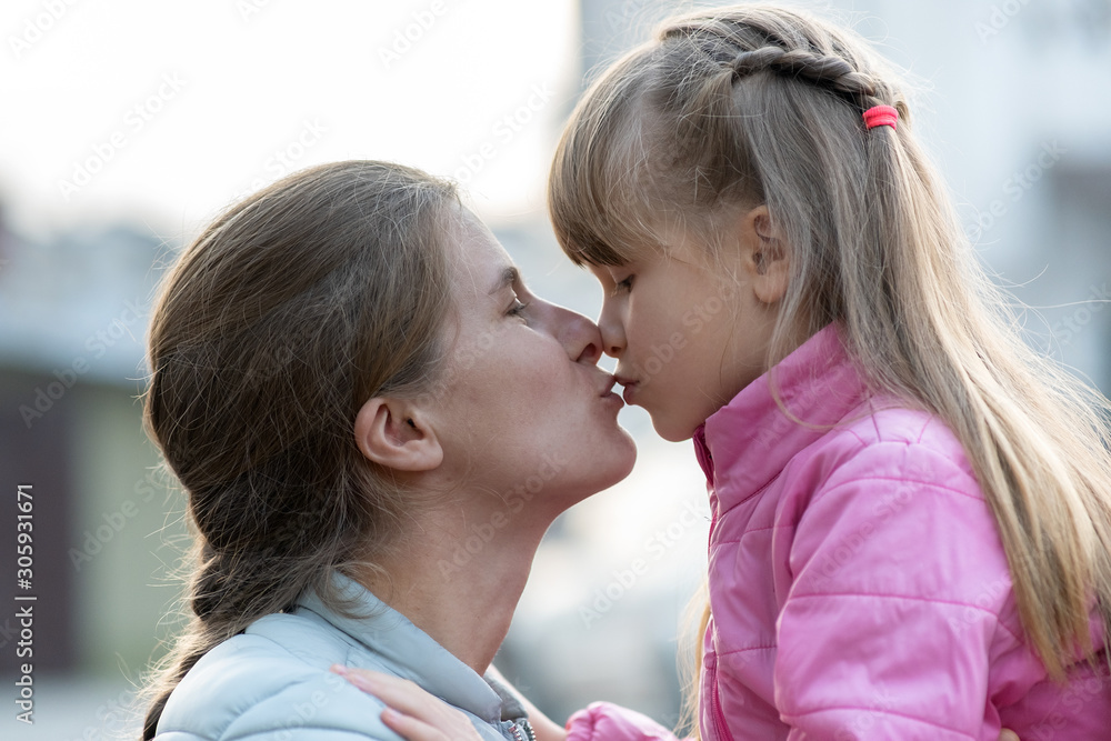 Happy mother and child daughter hugging together and kissing outdoors.