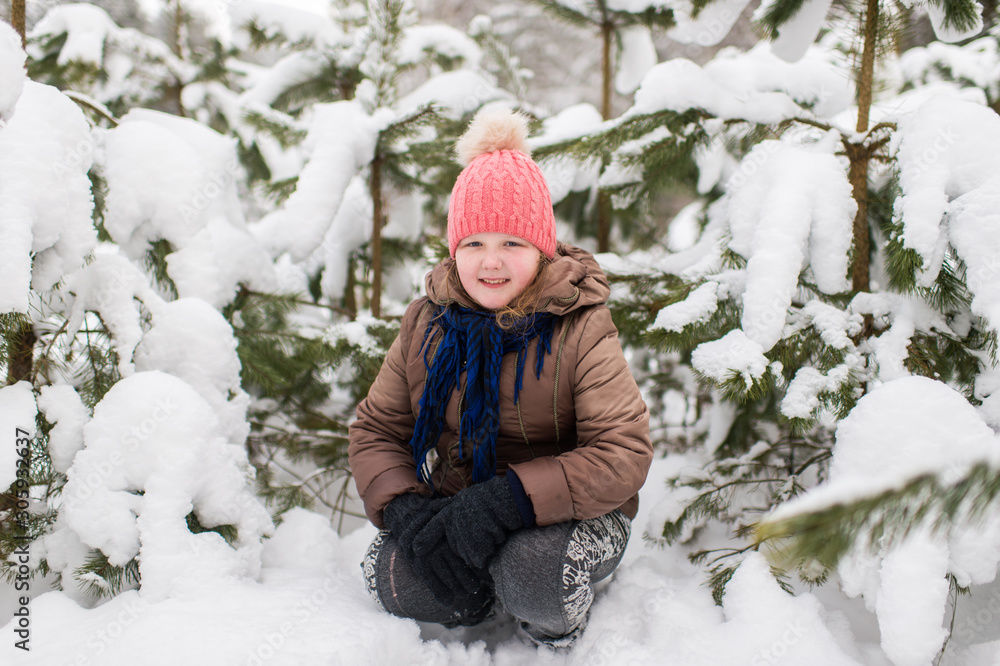 Happy little girl in winter clothes sitting outdoor under spruce tree covered with snow Happy little girl in winter clothes sitting outdoor under spruce tree covered with snow
