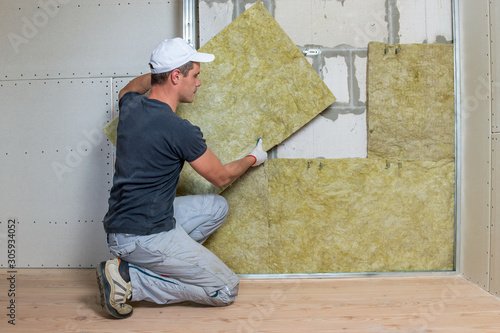 Worker insulating a room wall with mineral rock wool thermal insulation. photo