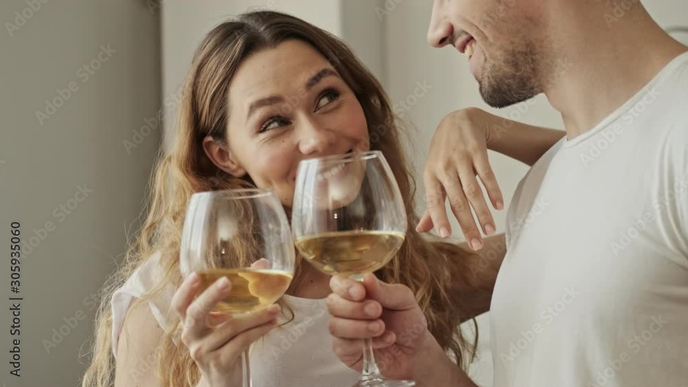 Cropped view of a young couple smiling while holding glasses and looking at each other in the apartment Cropped view of a young couple smiling while holding glasses and looking at each other in the apartment