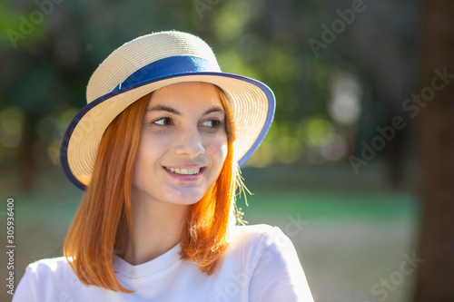 Closeup portrait of redhead hipster teenage girl in yellow hat smiling outdoors in sunny summer park. © bilanol