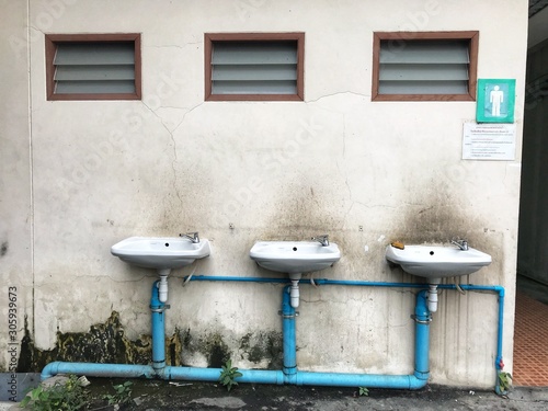 Three sinks and faucets are installed on the dirty wall with water conservation sign.