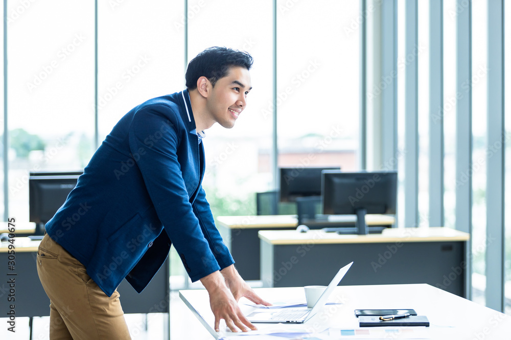 Portrait of a cheerful mature asian young businessman wear a business suit of man in blue shirt and laptop looking at the window In the office room background.