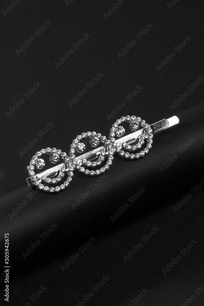 Subject shot of a silver hair clip made as three smiling emoji decorated with rhinestones on the black silky tube on the black background. Subject shot of a silver hair clip made as three smiling emoji decorated with rhinestones on the black silky tube on the black background.