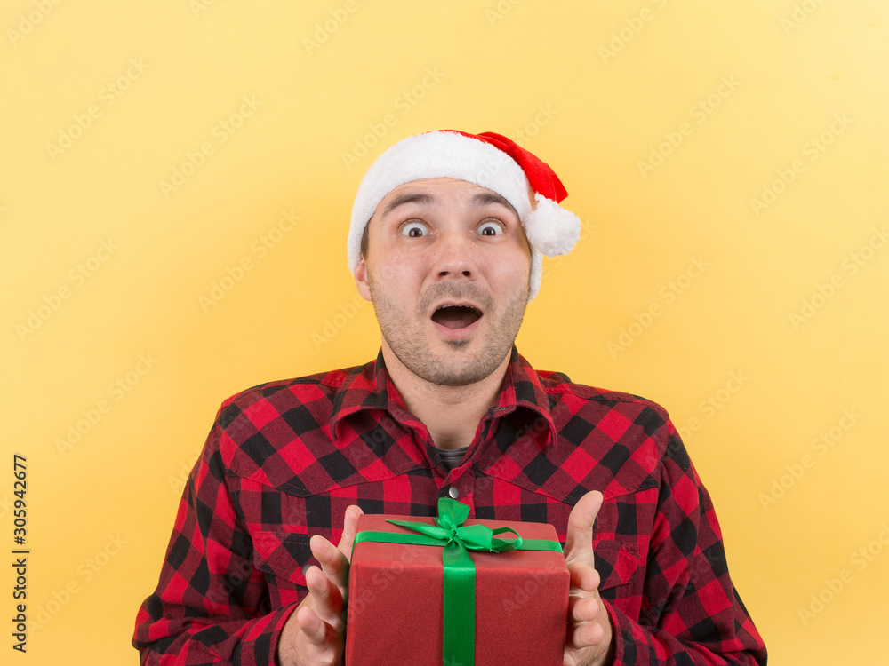 Happy surprised man in a red hat holding a gift with admiration on his face. Positive human emotions at christmas. Yellow background, copy space. Happy surprised man in a red hat holding a gift with admiration on his face. Positive human emotions at christmas. Yellow background, copy space.