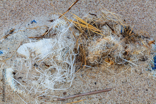 Environmental pollution - a big tangle of the rests of a worn big bag and its catches, lying on the beach as waste photo