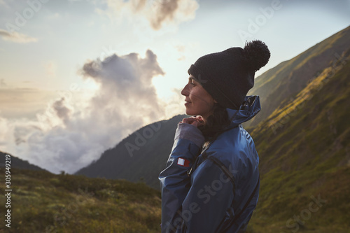 A young woman hiker in a blue jacket standing on view point in the mountains, clouds in a gorge on background. Caucasian nature reserve Sochi