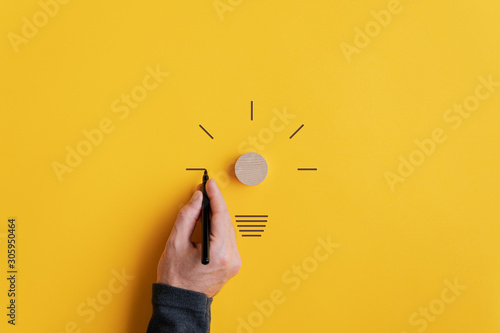 Male hand drawing a light bulb with black marker