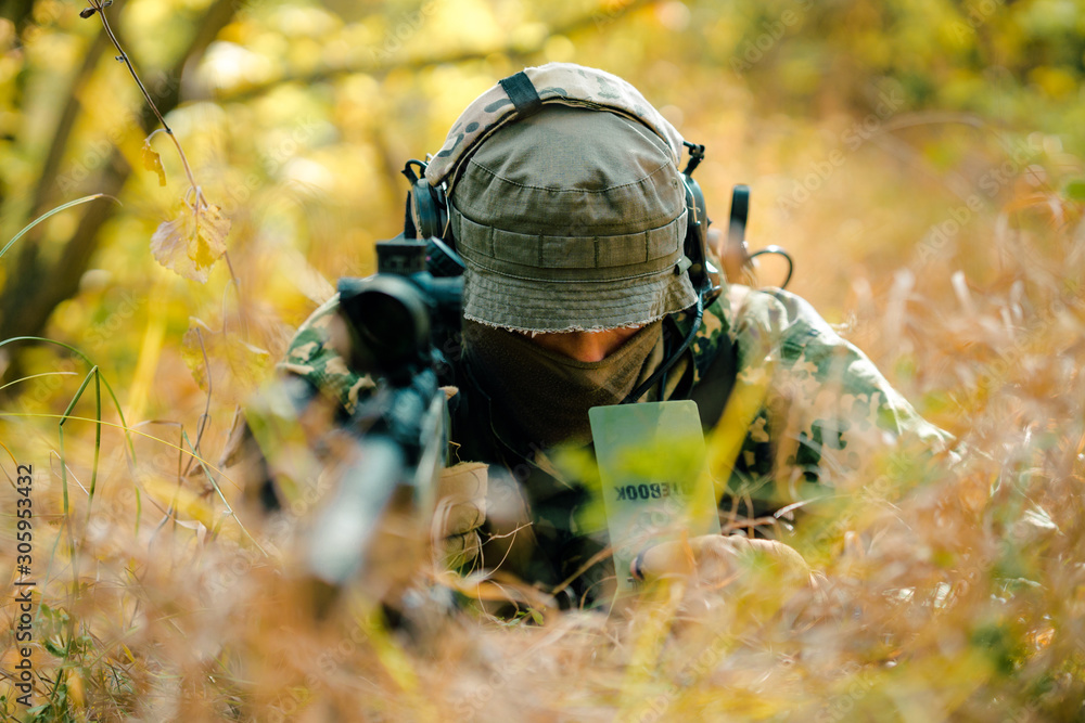 Closeup man in uniform with sniper rifle, front view. Airsoft soldier lay in long grass and check wind correction in note