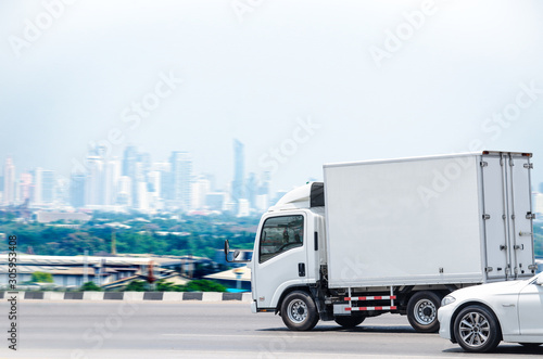 Fototapeta Naklejka Na Ścianę i Meble -  A small white truck running on the road for a transportation business with a city background.