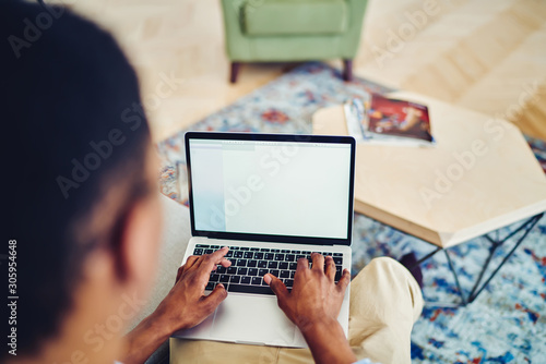 Cropped image of dark skinned male freelance typing on laptop computer with mock up screen doing remote job at home interior, man's hands keyboarding on netbook article publication for personal blog.