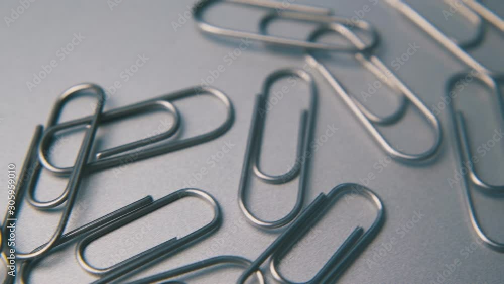 motion past small heap of shiny metal paperclips lying on clean grey surface extreme close view motion past small heap of shiny metal paperclips lying on clean grey surface extreme close view