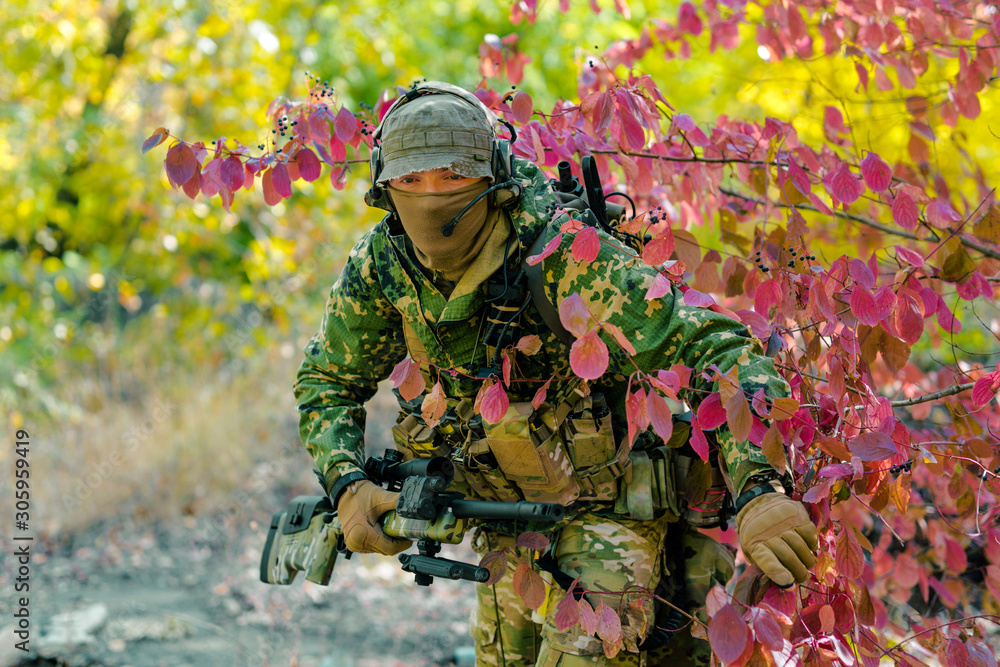 Man in green uniform with sniper rifle. Airsoft soldier stand in bush. Front view