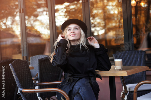 Young beautiful woman in hat sitting in a cafe and drinking a cappuccino.