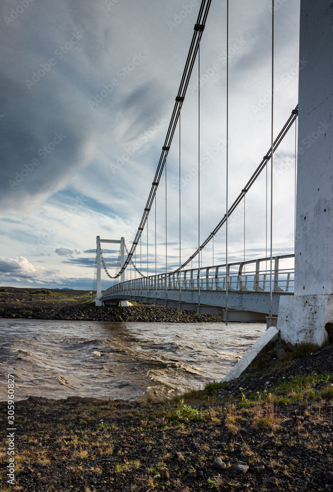 Obraz premium Small cable bridge empty road, suspension bridge crossing river, dramatic sky by the sunset
