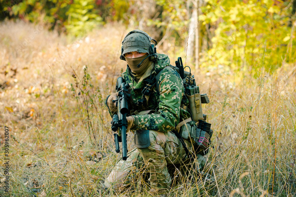 Airsoft man in uniform with sniper rifle, lurking in grass