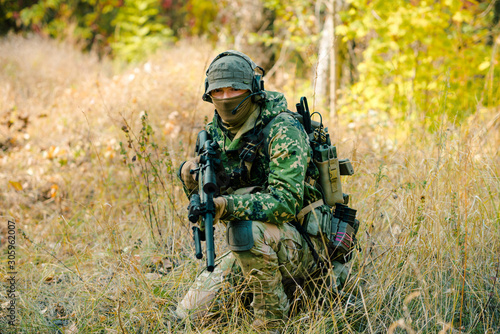 Airsoft man in uniform with sniper rifle, lurking in grass