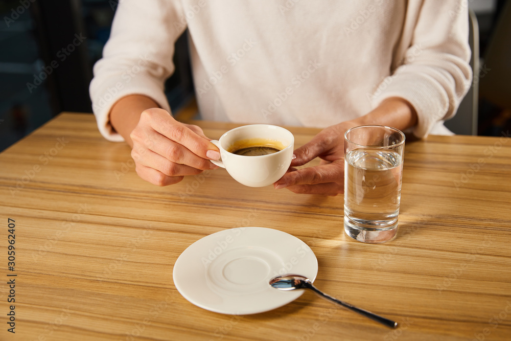 cropped view of woman holding cup of hot coffee near glass of fresh water in cafe cropped view of woman holding cup of hot coffee near glass of fresh water in cafe