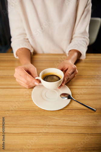 cropped view of woman holding cup of coffee in cafe