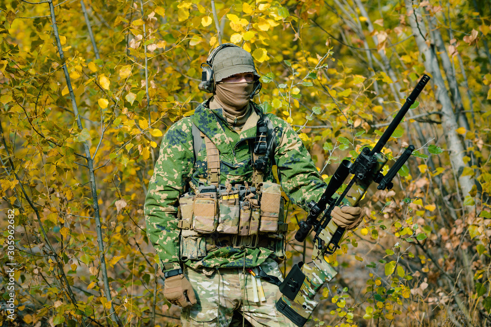 Airsoft man in uniform hold sniper rifle on yellow forest backdrop
