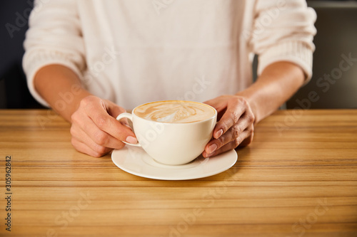 cropped view of woman holding cup of cappuccino