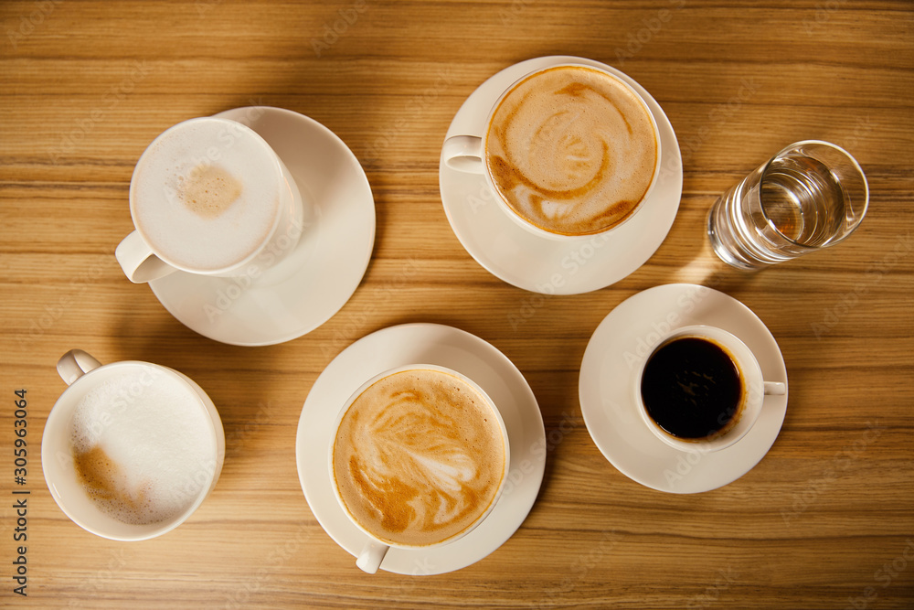 top view of saucers with cups of different coffee near glass of water top view of saucers with cups of different coffee near glass of water