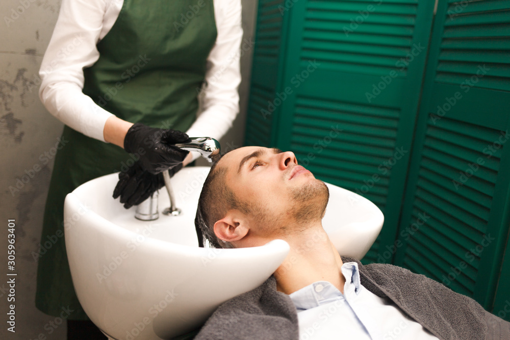 Hairdresser washes a client’s hair before cutting. Serious handsome man washes his head in a beauty salon Hairdresser washes a client’s hair before cutting. Serious handsome man washes his head in a beauty salon