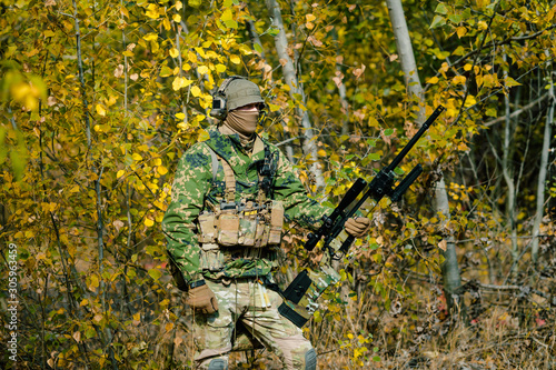 Airsoft man in uniform hold sniper rifle on yellow forest backdrop. Side view