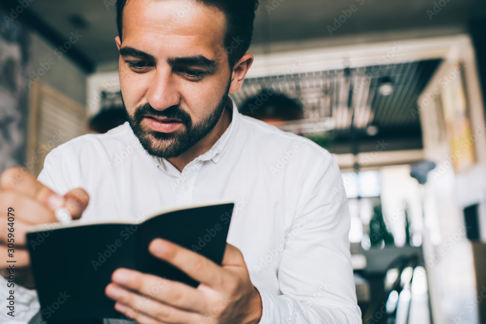 Experienced male manager creating checklist writing information to personal textbook concentrated on productive strategy for business startup project, Caucasian man accounting with notepad