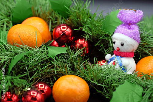 Ripe tangerines in artificial fir branches with Christmas balls and a toy snowman.