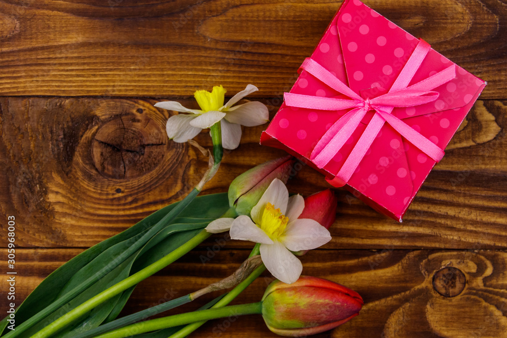 Fototapeta premium Gift box and bouquet of red tulips and daffodils on wooden background. Concept of Valentine's Day, Women's Day, Mother's Day and Birthday. Top view, copy space