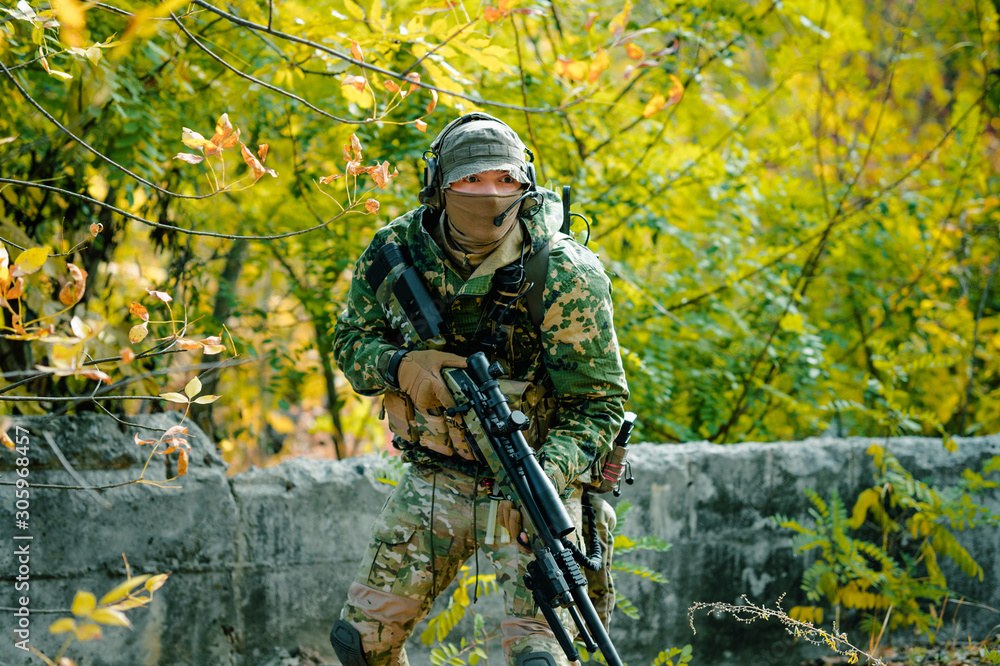Airsoft man in uniform hold sniper rifle on green forest background