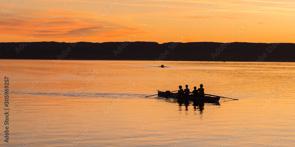 HERRSCHING, BAVARIA / GERMANY - Oct 11, 2019: The winners: Silhouette with row / rowing boat at sunset. Team of four people. Concept for achieving a target after hard work, endurance, coordination.