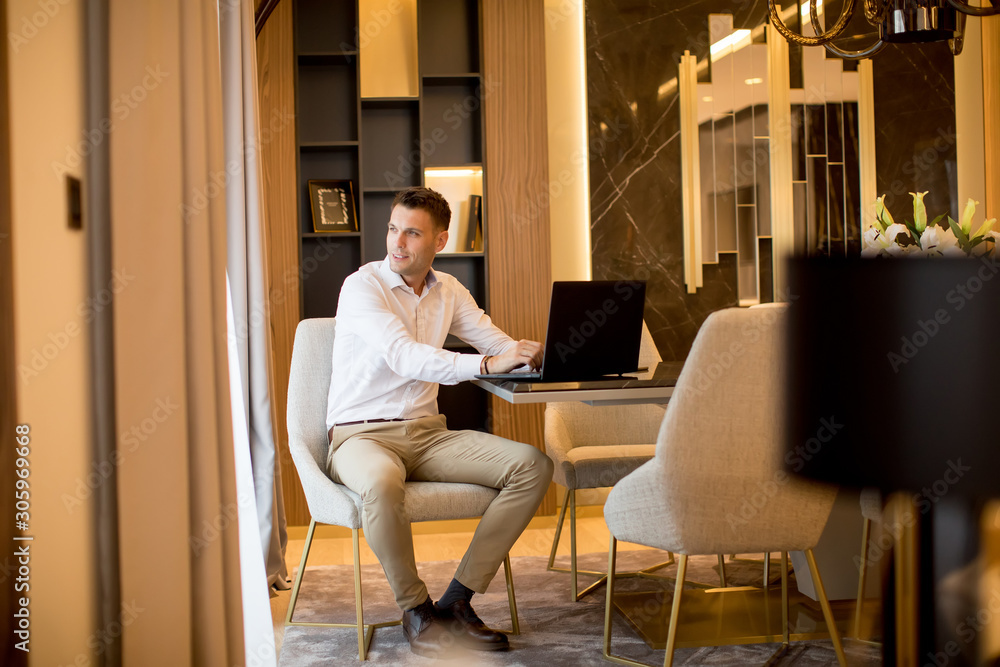 Young man sitting in a luxurious room in front of a laptop computer Young man sitting in a luxurious room in front of a laptop computer