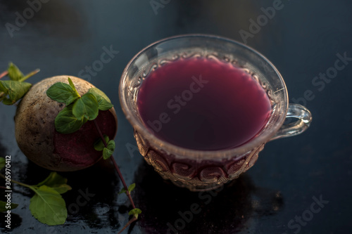 Best detoxify drink on a black glossy surface in a glass cup. Beetroot tea in a transparent glass cup on a black surface with a raw beet and some mint leaves. Horizontal shot with blurred background. photo