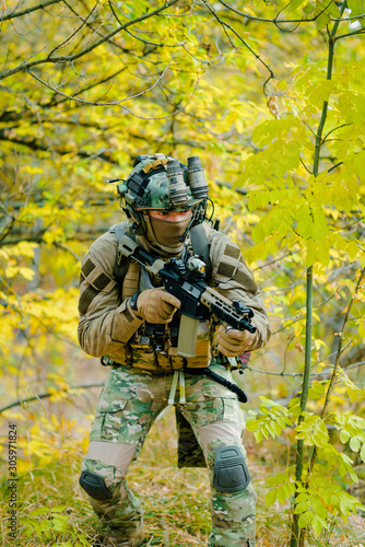 Airsoft man in uniform, move with machine gun on yellow forest backdrop. Vertical photo