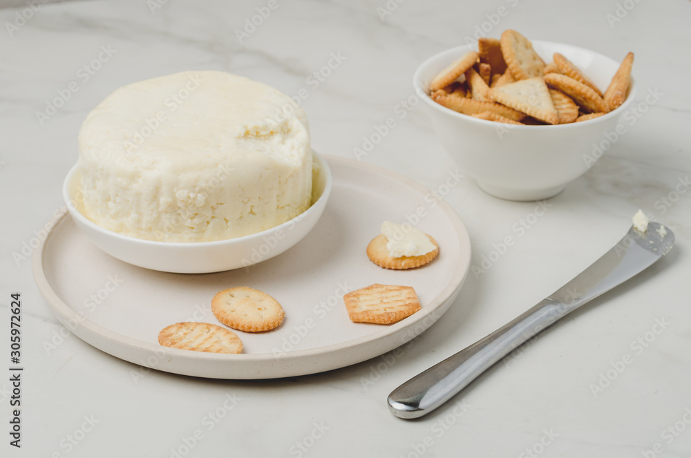 Cheese and cracker in a white bowl with a knife on a white table. Cheese and cracker in a white bowl with a knife on a white table.