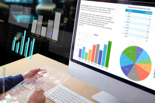 Business man or analyst in front of desktop computer holding a modern transparent tablet screen reviewing business performance and a return on investment, ROI, and investement risk analysis